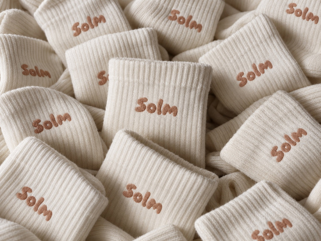 A pile of cream ribbed Solm socks with the Solm logo embroidered on each