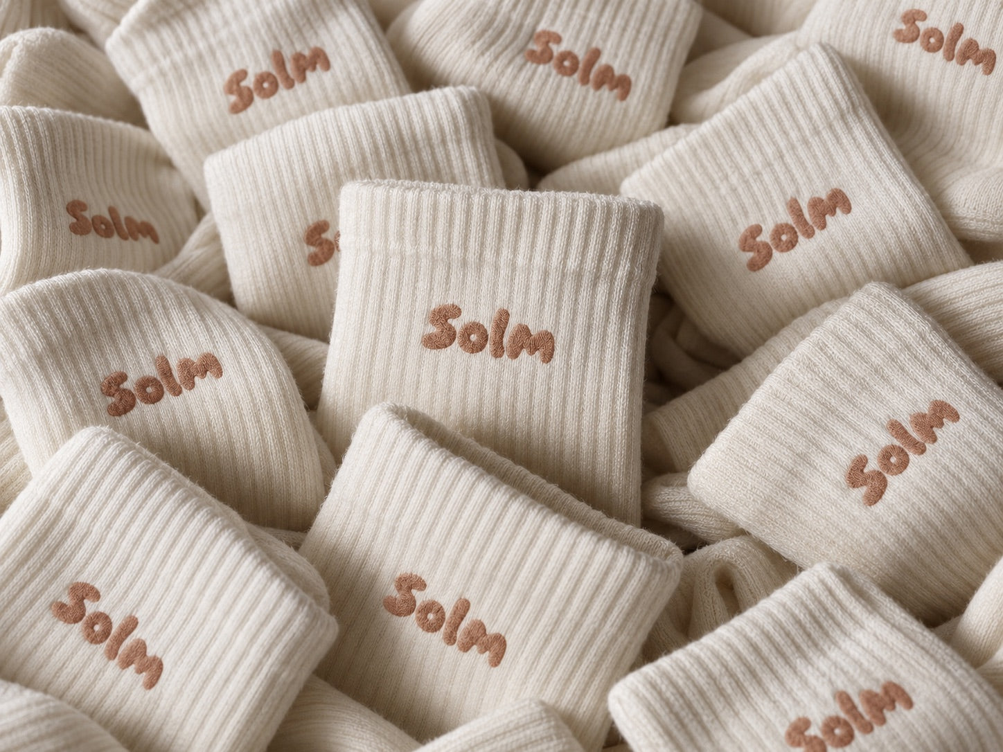 A pile of cream ribbed Solm socks with the Solm logo embroidered on each